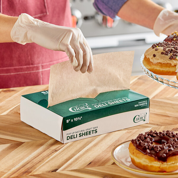A woman wearing gloves places a chocolate frosted donut in a natural kraft wax paper on a wood table.