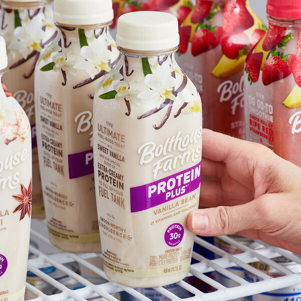 A hand holding a case of Bolthouse Farms Protein Plus Vanilla Bean shakes.