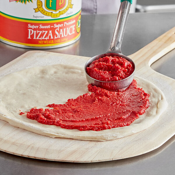 A spoon spreading Stanislaus Super Dolce Pizza Sauce on pizza dough.