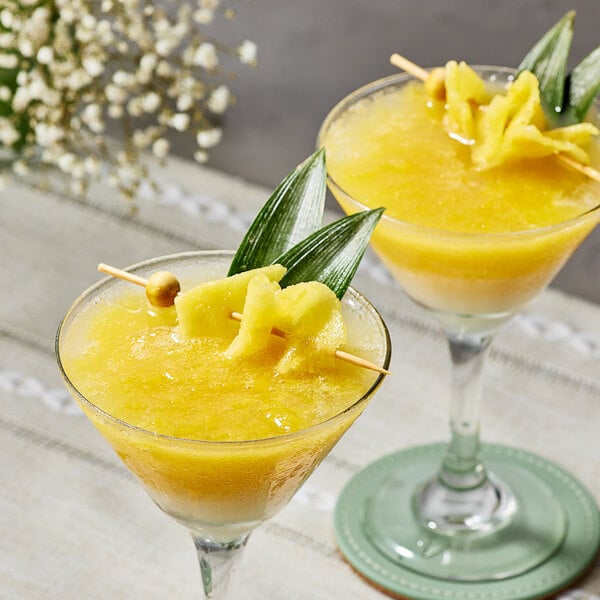 Two glasses of pineapple drinks with fruit on the rim.