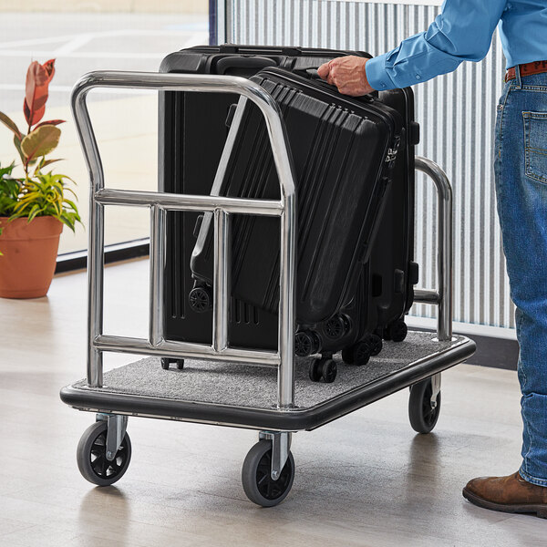 A person holding a Lancaster Table & Seating stainless steel luggage cart with a suitcase on it.