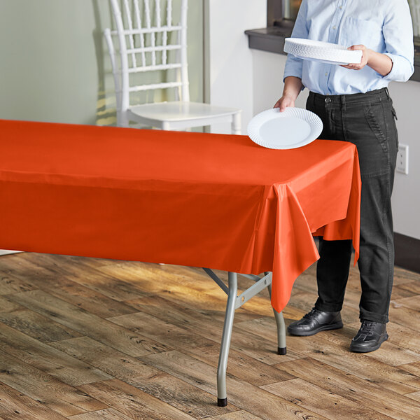 A woman standing next to a table with a tangerine plastic table cover holding a plate.