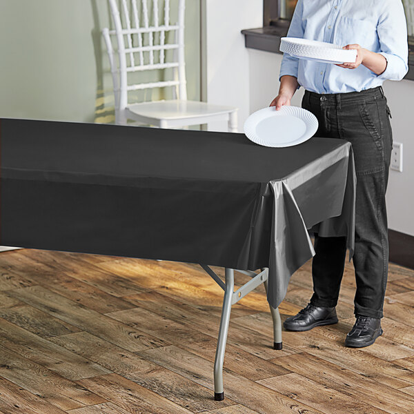 A woman standing next to a table with a black plastic table cover on it holding a white plate.