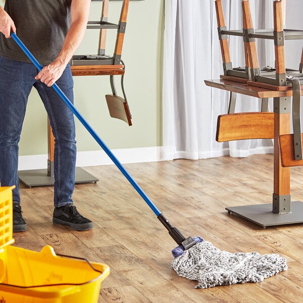 A man using a Lavex wet mop to clean a wooden floor.