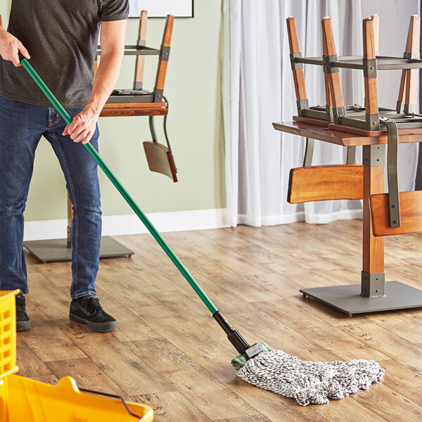 A man using a Lavex blue and white looped end wet mop on a floor in a professional kitchen.