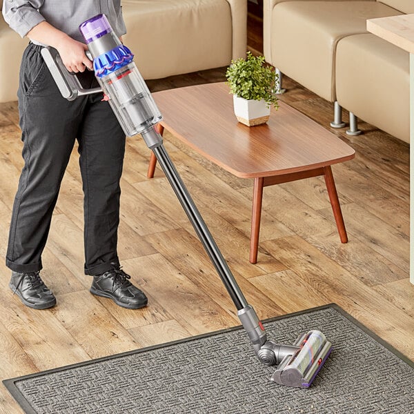 A person using a Dyson V15 Detect cordless stick vacuum to clean a rug.