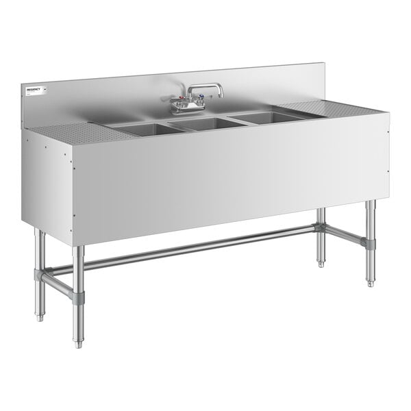 A stainless steel three-bowl sink with two side drainboards, a backsplash, and a central faucet, supported by metal legs.