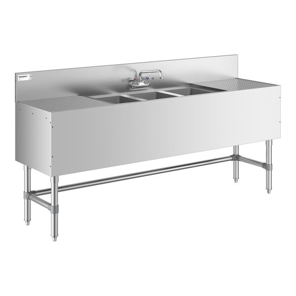 A large stainless steel sink unit with three deep basins, two side drainboards, a backsplash, and a central faucet, supported by metal legs.