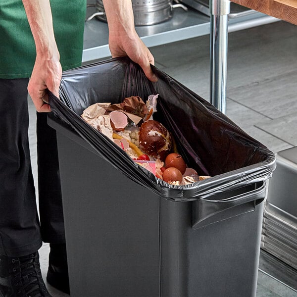 A person holding a black garbage bag over a trash can.