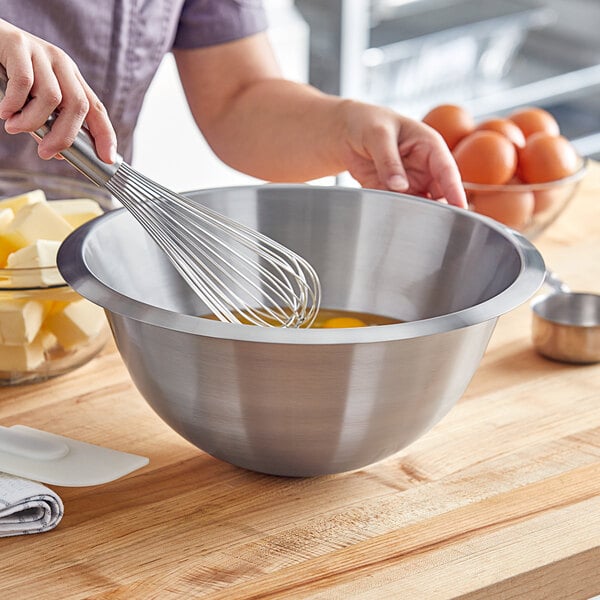 A woman whisking eggs in a Matfer Bourgeat stainless steel mixing bowl.