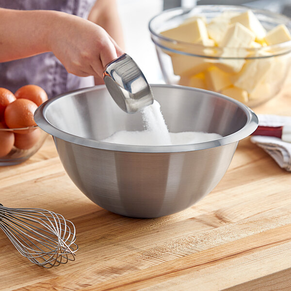 A person mixing eggs in a Matfer Bourgeat stainless steel mixing bowl.