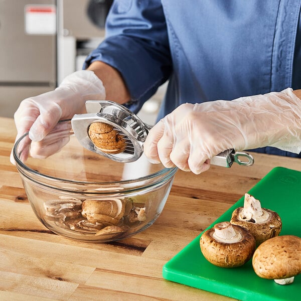 A person using a Louis Tellier stainless steel handheld mushroom slicer to slice mushrooms into a bowl.