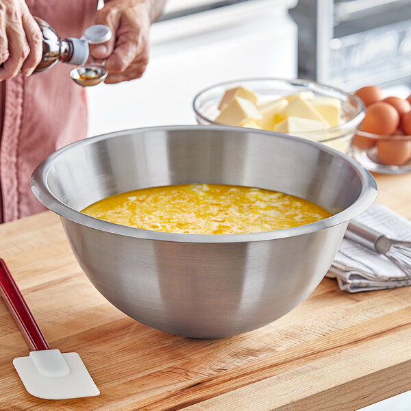 A person mixing eggs in a large Matfer Bourgeat stainless steel bowl.