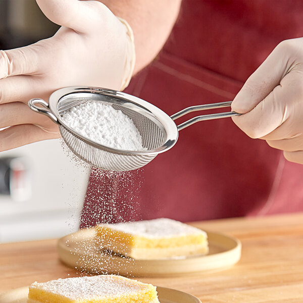A person using a Matfer Bourgeat fine mesh strainer to sift white powder onto a piece of cake.