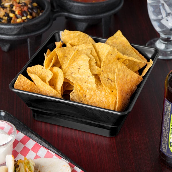 A black square plastic basket filled with chips on a table in a restaurant.