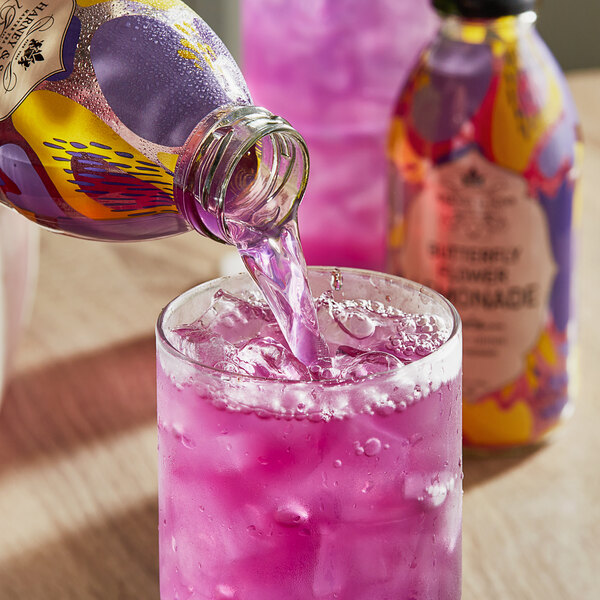 A glass of Harney & Sons Organic Butterfly Flower Lemonade being poured from a glass bottle