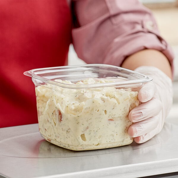 A person in gloves holding a Pactiv deli container of potato salad.