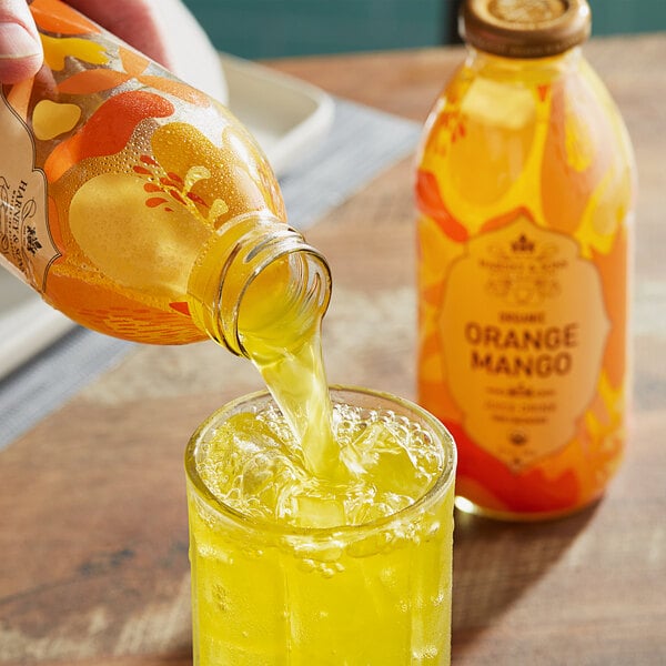 A hand pouring Harney & Sons Organic Orange Mango Juice into a glass.