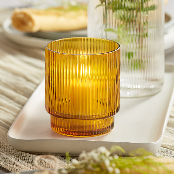 An Acopa Lore amber glass tealight holder with a lit candle on a tray.