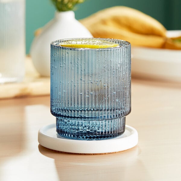 An Acopa Lore blue rocks glass with a lemon inside on a coaster.