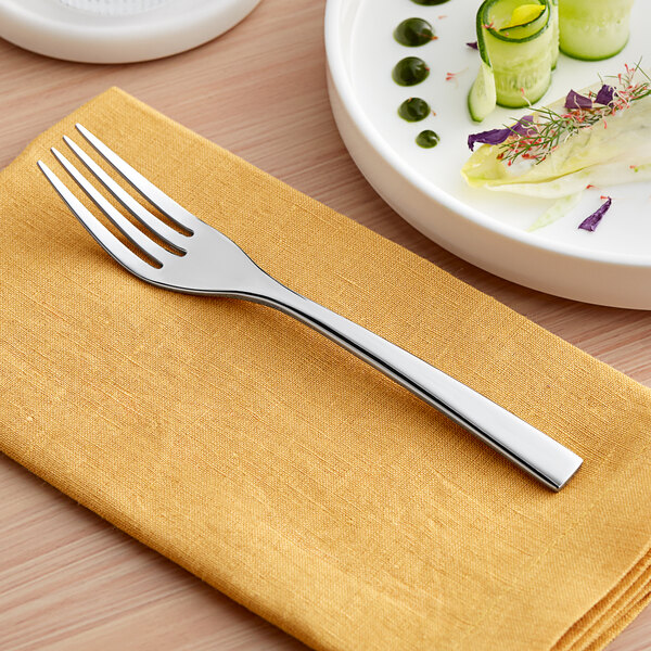 An Acopa stainless steel salad fork on a napkin next to a plate of food.