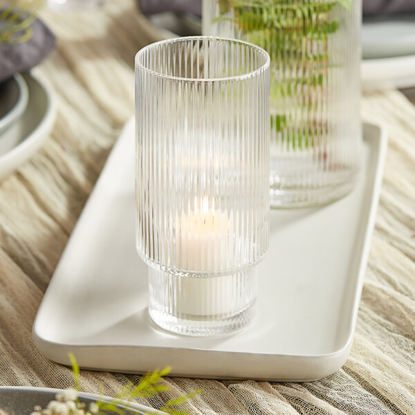 A clear glass Acopa Lore tealight holder on a tray with a candle.