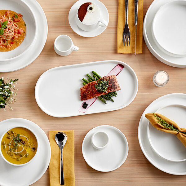 A table with white plates and Acopa Lore stainless steel dessert spoons.