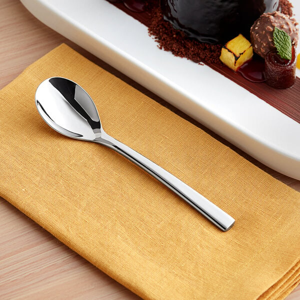 An Acopa stainless steel teaspoon on a table next to a plate of dessert.