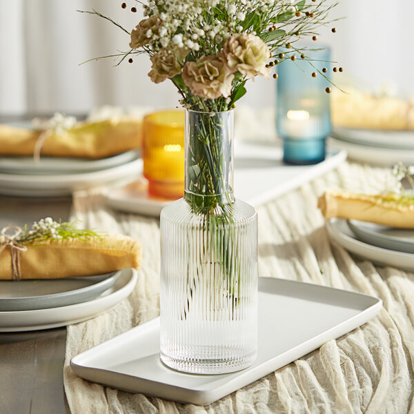 An Acopa Lore ribbed glass vase filled with flowers on a table.