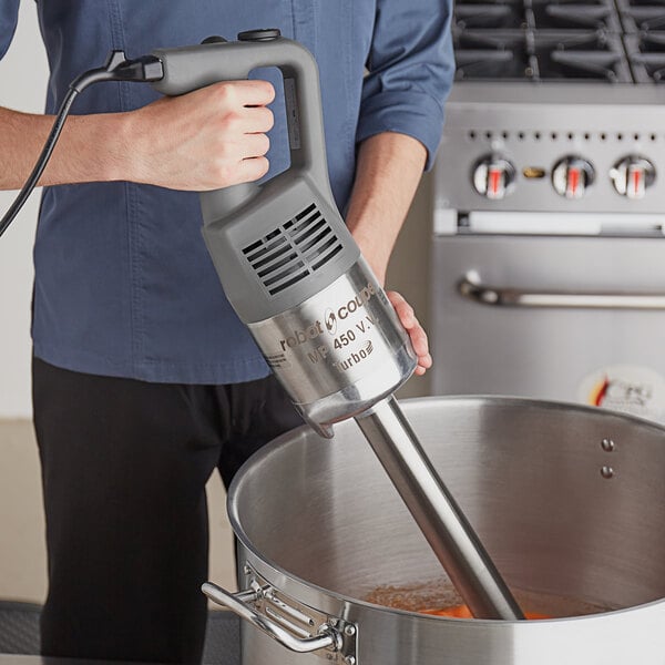 A person using a Robot Coupe immersion blender to mix soup in a pot.