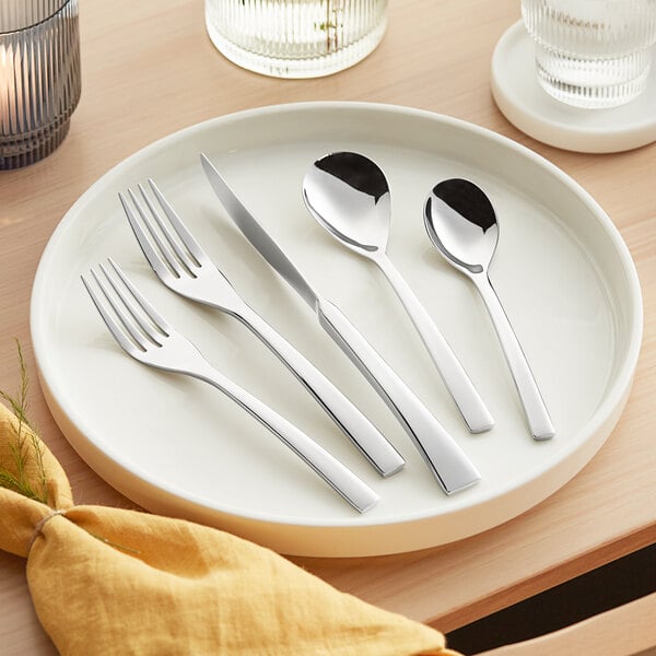 A white plate with Acopa Lore stainless steel flatware on it.