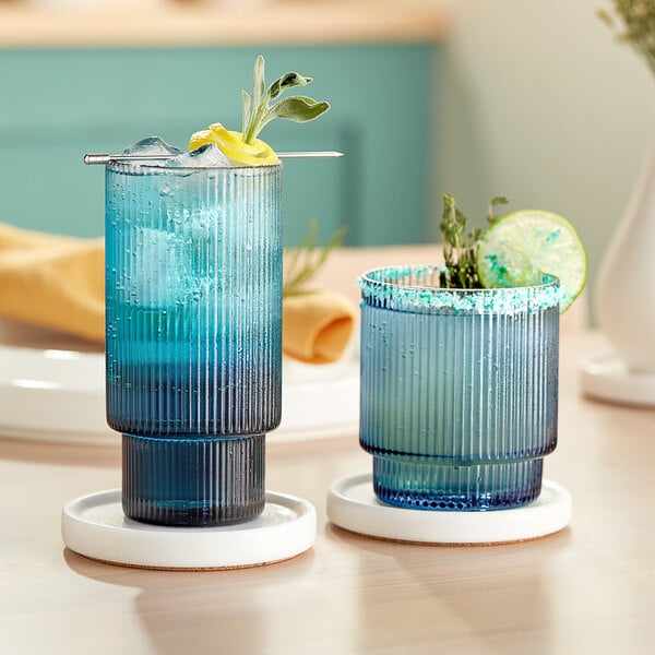 A pair of blue Acopa Lore rocks glasses on a table with a drink inside.