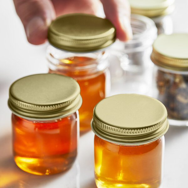 A hand holding a jar of honey with a gold metal lid.