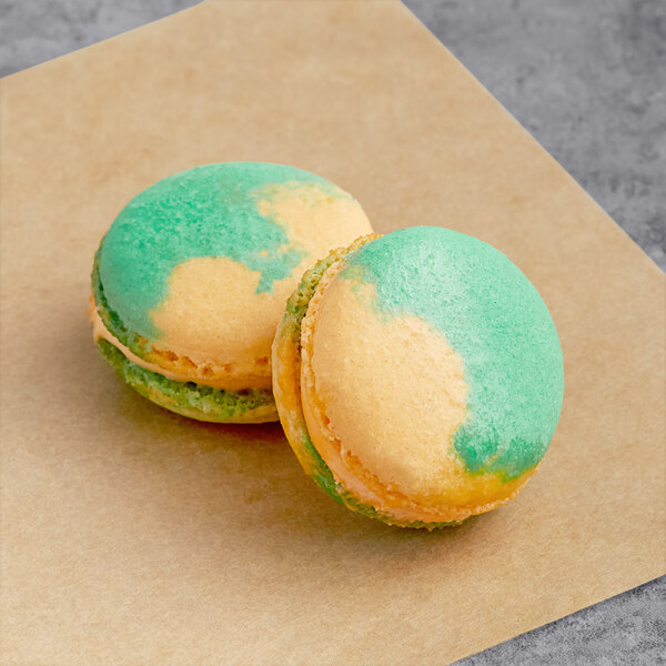 Two yellow and green Kumquat Macarons on a brown paper.