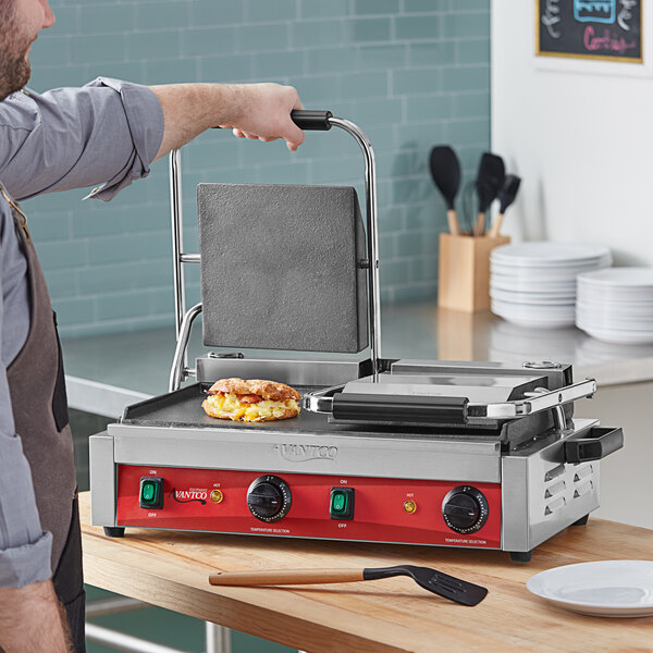 A man cooking a sandwich on an Avantco commercial panini grill.