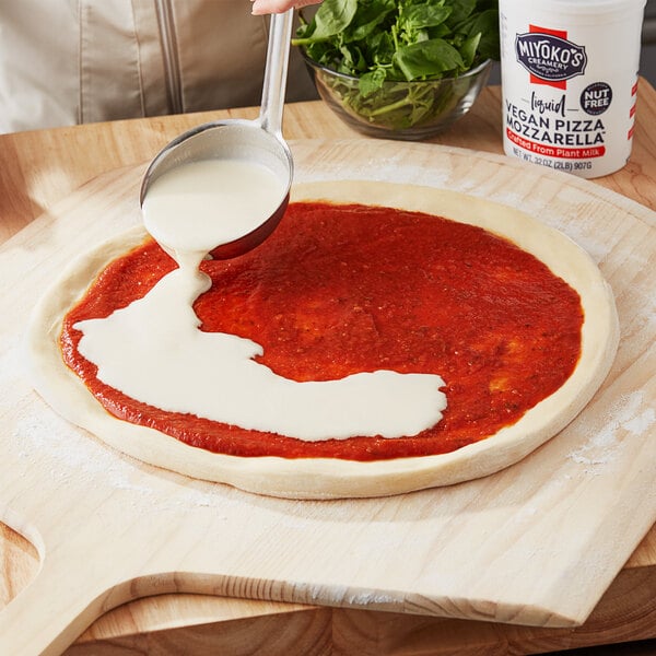 A person pouring white liquid from a white container onto a pizza.