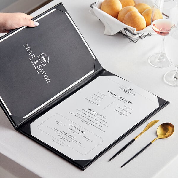 A hand holding an open black Acopa Prime menu on a table with food and glasses.