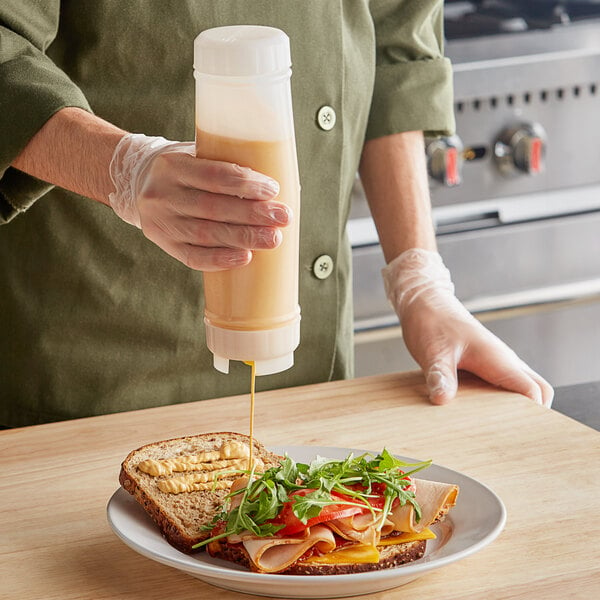 A person pouring San Jamar sauce onto a sandwich.