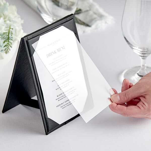 A close-up of a hand holding a menu card with a wine glass on a table.