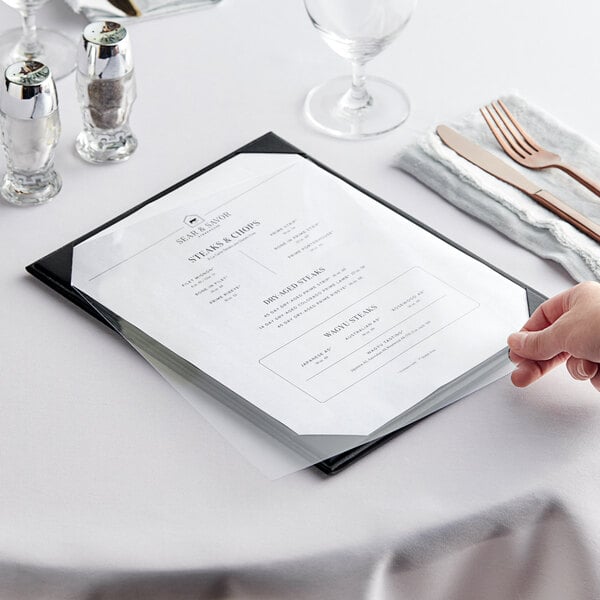 A hand holding an Acopa clear vinyl menu on a table.