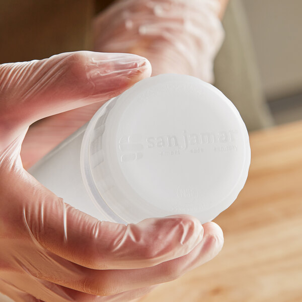 Plastic gloved hands using a San Jamar solid cap on a plastic container.