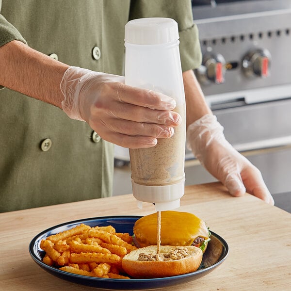 A person using a San Jamar sauce bottle to pour sauce onto a plate of food.