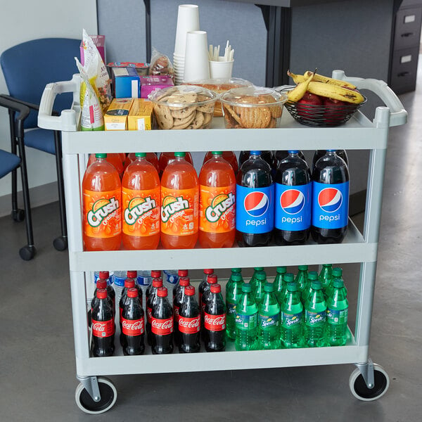 A Cambro speckled gray utility cart with shelves holding drinks and snacks.