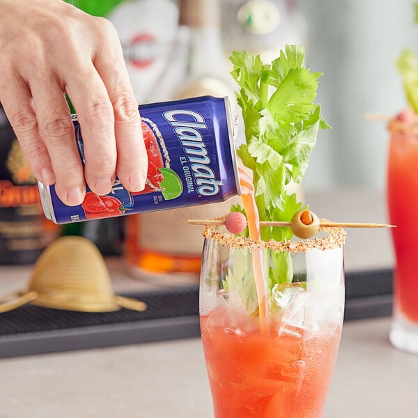 A hand pouring Clamato Original Tomato Cocktail from a blue can into a glass.