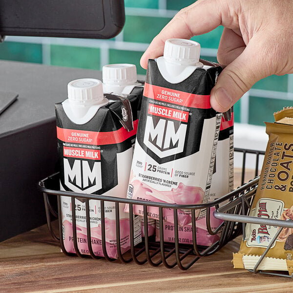 A hand holding a small black carton of Muscle Milk Strawberries 'n Creme protein shake.