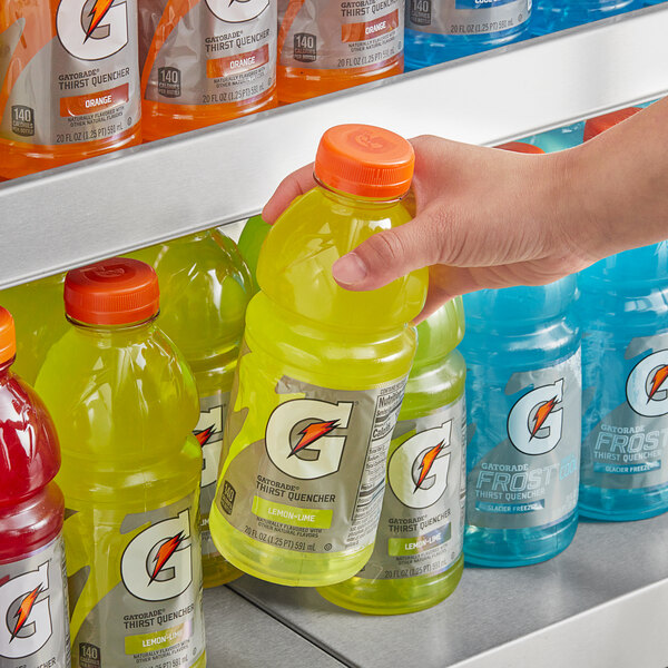 A hand holding a bottle of yellow Gatorade Thirst Quencher lemon lime sports drink.