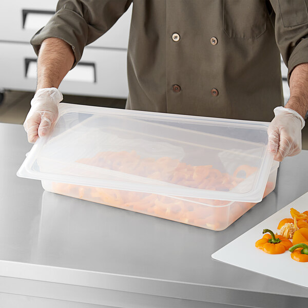 A man in a chef's uniform using a Cambro translucent polypropylene seal cover on a plastic container of food.