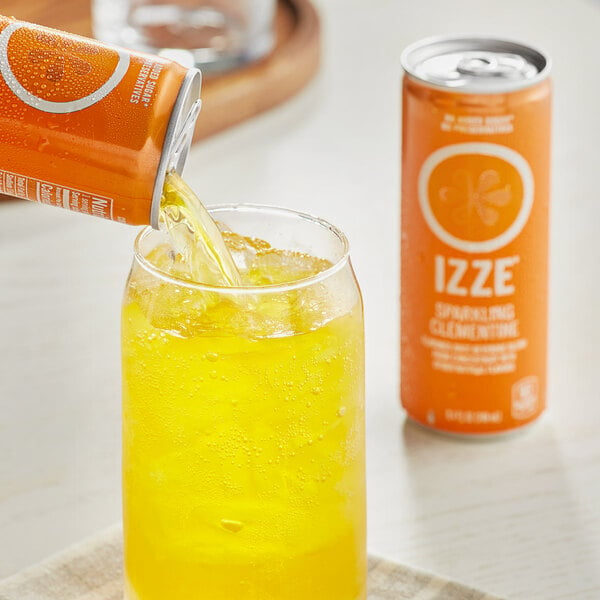 A hand pouring Izze Clementine sparkling juice from a can into a glass of ice.
