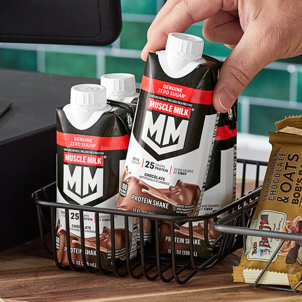 A person holding a black rectangular carton of Muscle Milk Chocolate Protein Shake.