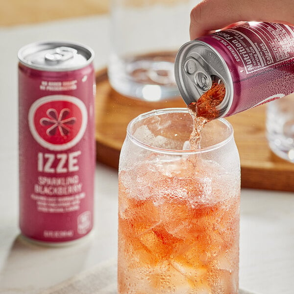 A hand pouring Izze Blackberry Sparkling Juice from a red and white can into a glass with ice.